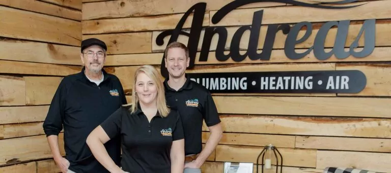Three Team Andreas staff posing in their office. Team Andreas logo in black on wall behind them. Staff all wearing black Andreas polos.
