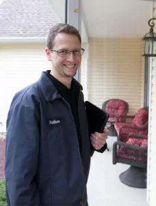Andreas HVAC technician smiling while standing in front of a home, holding a notepad in one hand.