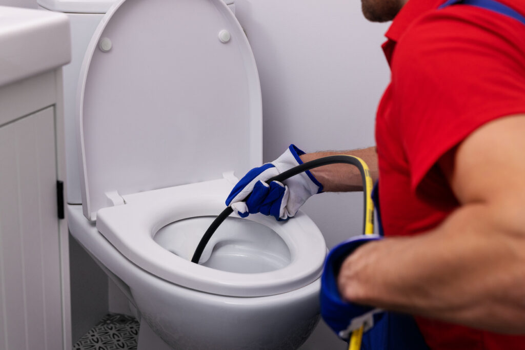 plumber unclogging blocked toilet with hydro jetting in home bathroom.