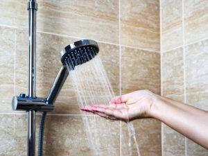 A hand testing the temperature of the water in a shower.