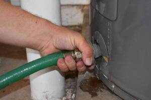 A person connecting a hose to a water heater tank.